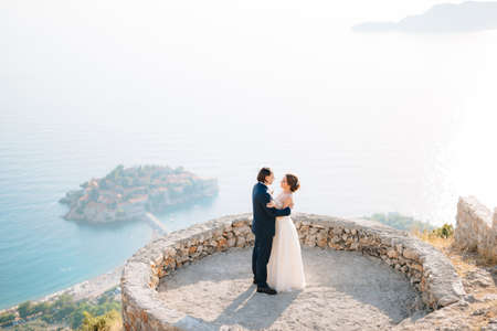 The bride and groom embrace on the observation deck overlooking the island of Sveti Stefanの写真素材