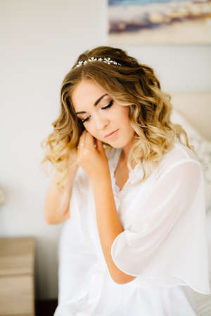 Bride wearing white peignoir puts on an earring while preparing for the weddingの写真素材