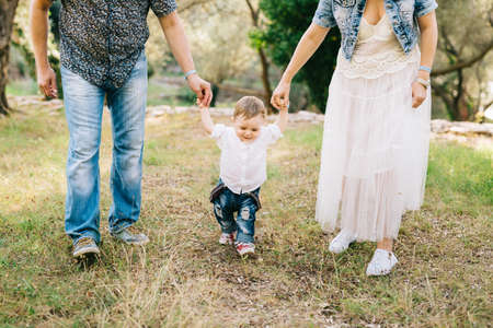 Happy family - mom and dad hold little son by the arms in the olive grove, close-up