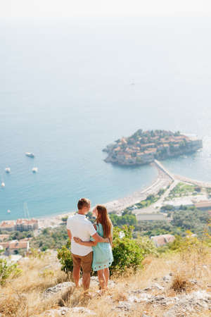 A man and a woman stand embracing on a mountain overlooking the island  and look at each otherの写真素材