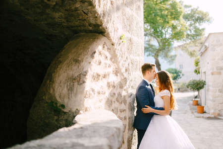 The bride and groom hug on a beautiful old street of Perast, the groom kisses the bride on the foreheadの写真素材