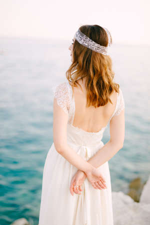 The bride stands on the seashore with her hands folded behind her back and looks into the distanceの写真素材