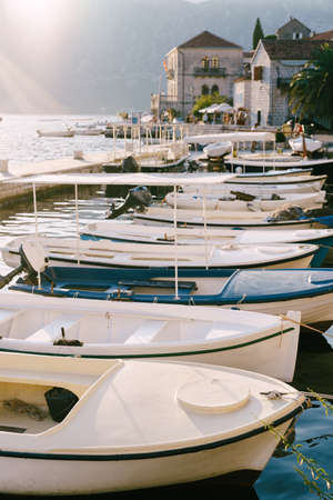Fishing boats at the pier with houses in the background on a sunny day in Perast, Montenegro.