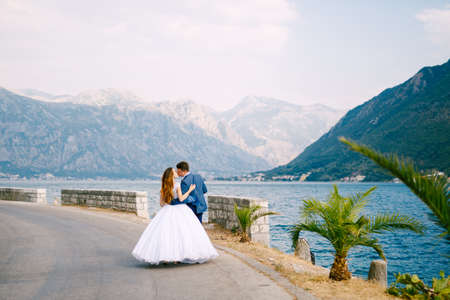 The bride and groom walk along the road near Perast and kiss, back viewの写真素材