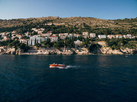Luxurious wooden boat with a motor sails on the background of the coast near the old town of Dubrovnik and Villa Sheherezade. Villas and hotels on the coast of Croatia.の写真素材
