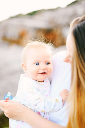 Portrait of an adorable baby girl in her mothers arms at a rocky beach