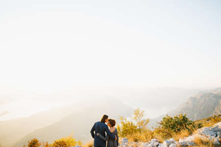 The bride and groom embracing and kissing on the Lovcen mountain behind them opens a view of the Bay of Kotor, back viewの写真素材
