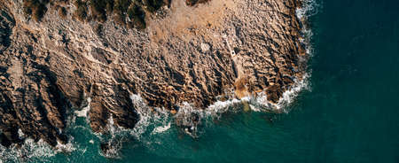 Dramatic marine background. Rocky coast of the Adriatic Sea. White foamy waves beat against the stone shore. Panorama of the sea coast. Aerial top view.の写真素材
