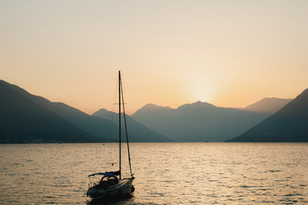 Silhouette of a moored sailing yacht against the background of the setting sun over the mountains. Fiery yellow sunset over the mountains in the Bay of Kotor in Montenegro.の写真素材