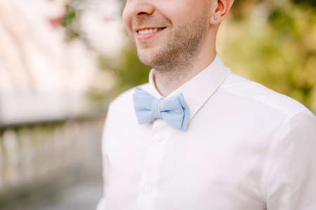 A man in a white shirt and a blue bow tie smiles on a sunny day, close-upの写真素材