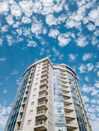 A multi-storey circular building with blue windows against a background of blue sky and white clouds.の写真素材