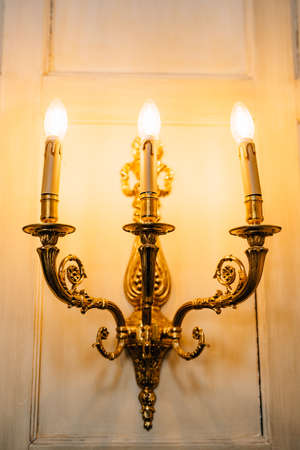Gold three-lamp floor lamps, decorated with floral patterns on the wall. Interior details of an old villa in Italy.の写真素材