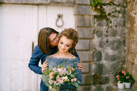 The groom kisses the bride on the cheek against the background of an old building with white doors in the old town of Perastの写真素材