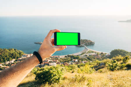 Man holds horizontally in his hand a smartphone with a blank screen against the background of islandの写真素材