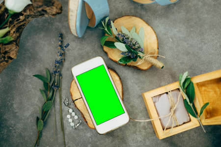 Smartphone with a blank screen lies on a beautiful wooden stand next to a jewelry box, flowers and...