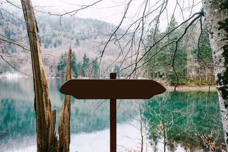 Unmarked road sign stands near a lake in the forest against a background of mountainsの写真素材