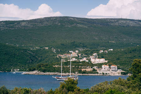 White sailing schooner sails along a blue bay against the backdrop of green mountains and an ancient cityの写真素材
