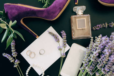 Lilac high heel shoe, a bottle of perfume, a smartphone, jewelry and flowers on a green backgroundの写真素材