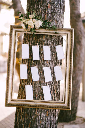 Blanks for the wedding guest list hang in a beautiful frame on a tree. Seating planの写真素材