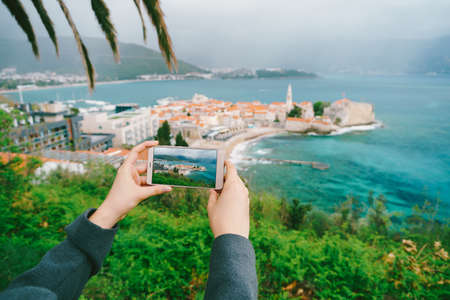 Man holds a smartphone with a photograph. In the background - the old town of Budva in the fog, Montenegro.の写真素材
