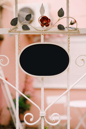 Empty oval sign on the background of a beautiful forged white fence with flowersの写真素材