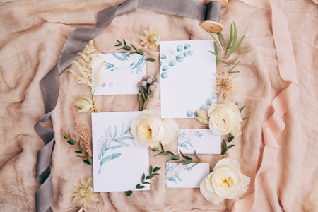 Watercolor paintings, ribbons, roses, green twigs and wildflowers lie on a beautifully spread canvas. The pictures show the stems of flowersの写真素材