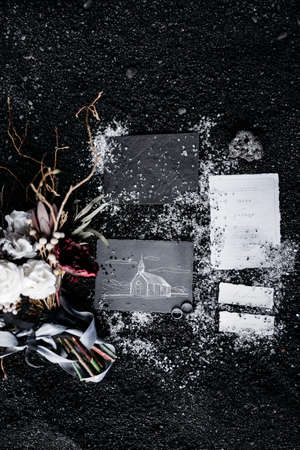 On the black ground lie wedding rings, gray and white cards, a bouquet of flowers, ribbon and colored pencils. The postcard depicts a white church on a black backgroundの写真素材