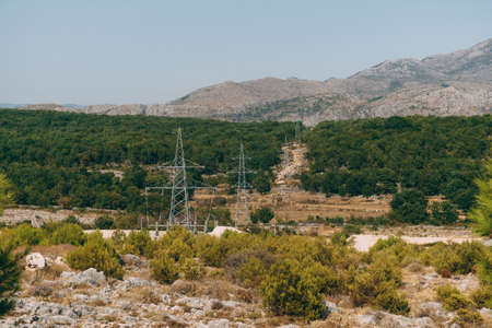 Electrical pylons of power lines in the forest against the background of mountainsの写真素材