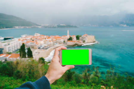 Hand holds a phone with a blank screen. The old town can be seen in the distanceの写真素材