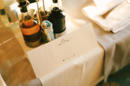 Blank invitation stands on a table covered with a white tablecloth. There are bottles of drinks aroundの写真素材