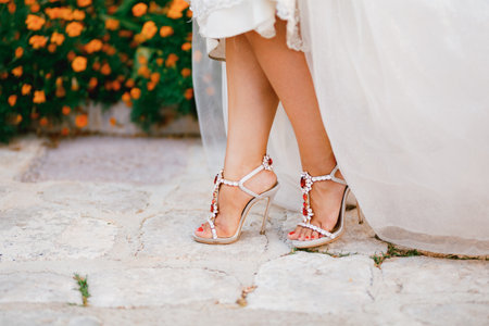 Brides legs in stylish sandals with crystals with high heels peek out from under the wedding dress, close-upの写真素材