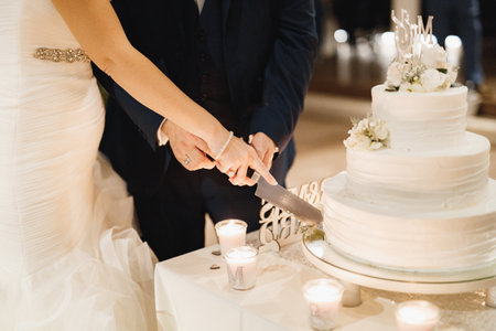 Bride and groom cutting three-tiered cake in white frosting together at a wedding party, close-upの写真素材