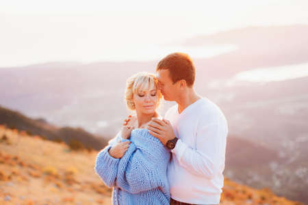 Man hugs woman in a blue sweater by the shoulders against the background of Mount Lovcen