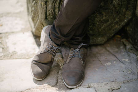 Groom stands in lace-up shoes on the cobblestone pavementの写真素材