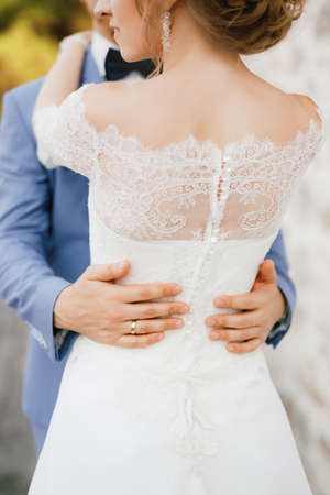 The bride and groom hug, the grooms hands on the waist of the bride in a lace dress, close-up