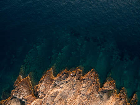 The bride and the groom lie hugging on a rocky shore, in front of them is a deep blue sea, top view