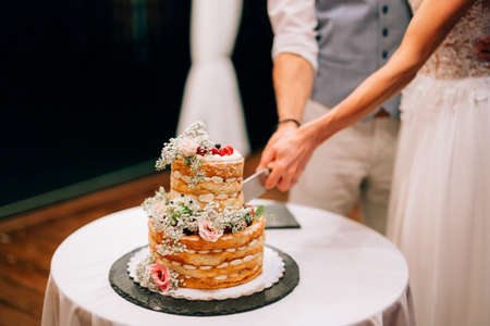 Bride and groom cut together a two-tiered wedding cake decorated with flowers and berries at a wedding banquetの写真素材