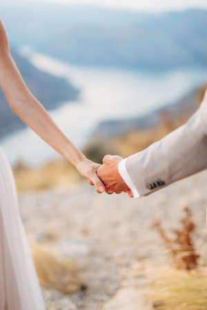 The bride and groom stand on Mount Lovcen overlooking the Bay of Kotor and hold each others hands, close-upの写真素材