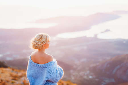 Woman in a blue sweater stands and looks at the panorama of Mount Lovcen, Bay of Kotor. Back viewの写真素材