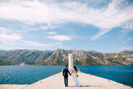 Beautiful bride and groom holding hands walk along the pier on a sunny summer dayの写真素材