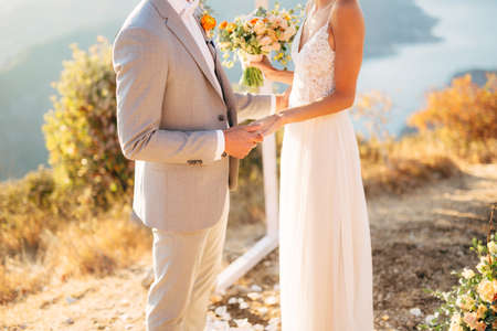 The bride and groom are standing on Mount Lovcen near the wedding arch and holding handsの写真素材