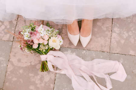 The brides legs in graceful white shoes peek out from under the skirt, next to the brides bouquet lies, close-upの写真素材