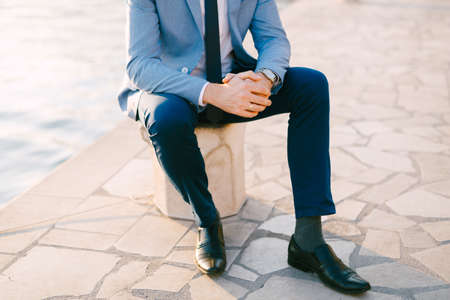 Half-portrait of man in a grey suit sitting on the embankment near the waterの写真素材