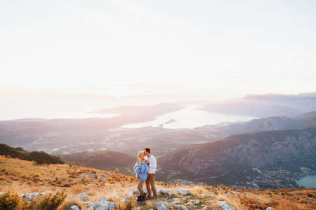 Man hugs a woman in a blue sweater by the shoulders against the background of Mount Lovcen, Kotor...