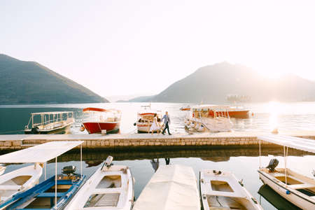 Groom and bride walk along the pier on the coast of the bay past the parked yachtsの写真素材