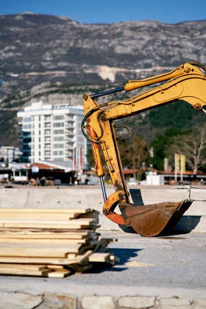 Yellow excavator bucket at construction site near wooden planks on background of finished house and mountainsの写真素材