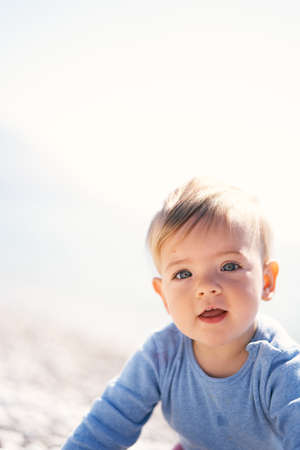 Cute baby is sitting on a pebble beach. Close-up. Portraitの写真素材