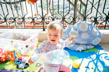 Laughing kid sits on a colored rug on the balcony near a plastic box with colorful toysの写真素材