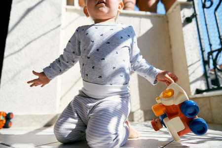 Little kid sits on his knees on the balcony and holds a toy car in his hand