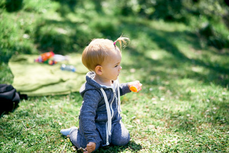 Little girl sits on a green meadow with a ball in her hand. Side view